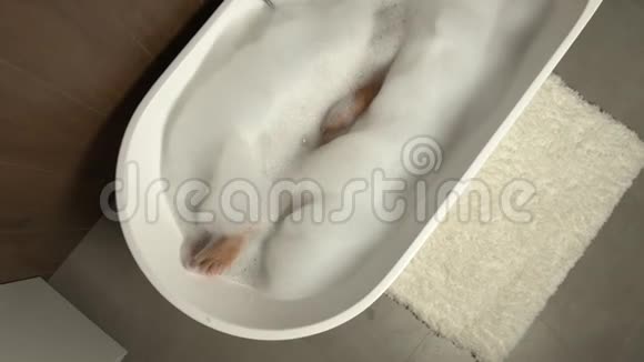 美丽的双腿躺在独立的浴缸里泡沫可以放松视频的预览图