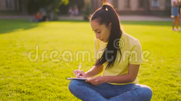 柔和的光线专注的女学生坐在公园里做作业4K视频的预览图