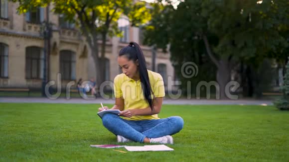 女学生20岁坐在草地上在笔记本上做笔记4K视频的预览图