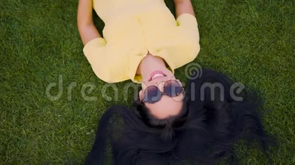 戴太阳镜的快乐女孩躺在草地上享受生活4K视频的预览图