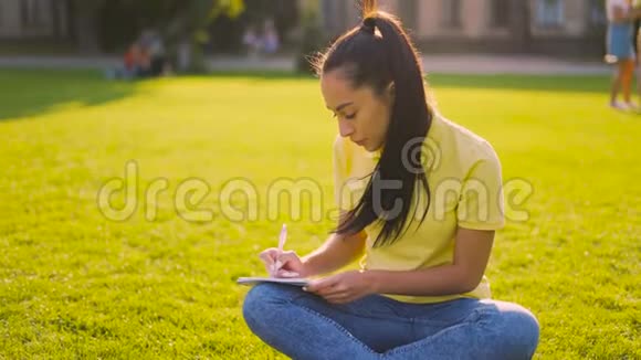 20岁的女孩坐在草地上在笔记本上做笔记4K视频的预览图