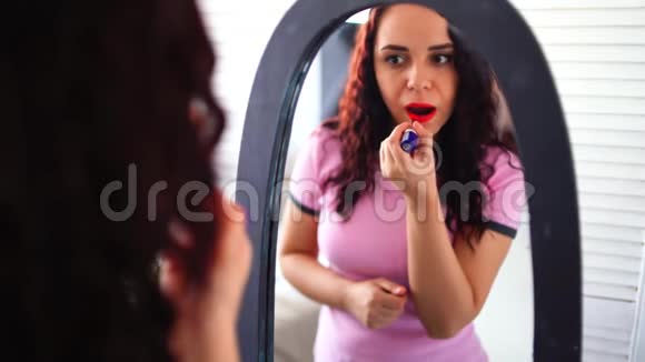 年轻漂亮的女人穿着睡衣在家照镜子涂着红色的口红与迷人的女性亲密接触视频的预览图