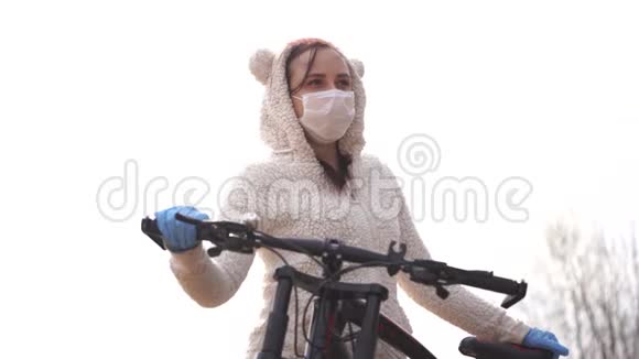 戴着医用口罩和手套的年轻女子骑自行车对抗天空的肖像成年女性面部保护视频的预览图