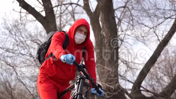 农村骑自行车的戴着医用口罩和手套的年轻人男性在散步时保护自己免受疾病的侵袭视频的预览图