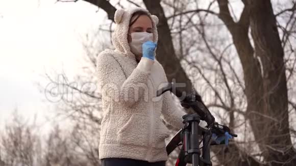 戴着医用口罩和手套的年轻女子咳嗽着手握着农村自行车的舵保护妇女视频的预览图
