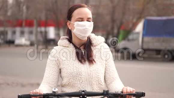 戴着医疗面具的年轻女子骑着自行车站在城市街道上成年女性戴面膜保护自己视频的预览图