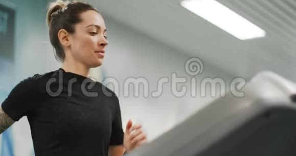 年轻女子在健身房跑步机上跑步前景近景上身细节健身中心女子训练视频的预览图