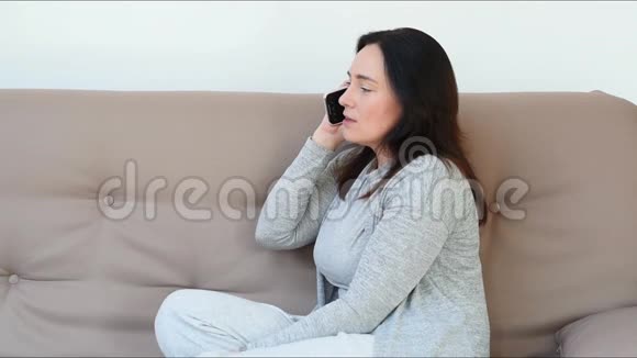 30多岁的年轻女子坐在沙发上在家打电话戴着灰色衣服的白人女人微笑着在电话里说话视频的预览图