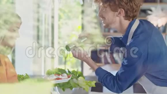男人把胡椒放在沙拉上年轻人一起做饭准备午餐或晚餐在家中露天厨房视频的预览图