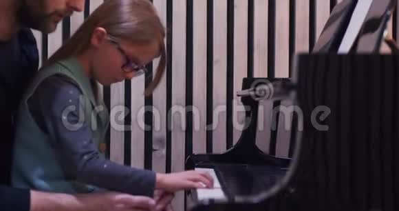 爸爸给女儿教钢琴小女孩在家学钢琴侧视家里的钢琴课儿童学习视频的预览图