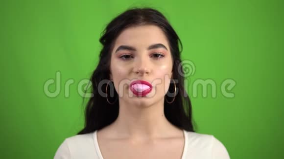 有趣的微笑女孩嚼着泡泡糖在绿色的屏幕上吹着粉红色的泡泡糖视频的预览图