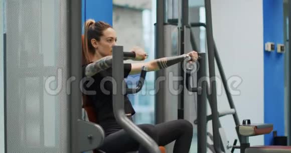 女性在胸部按压机上锻炼女子训练在健身房机器侧视中镜头女人在压杠视频的预览图