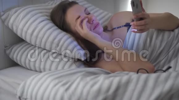 戴眼镜的女人躺在床上用智能手机她揉眼睛因为她又累又困概念视频的预览图