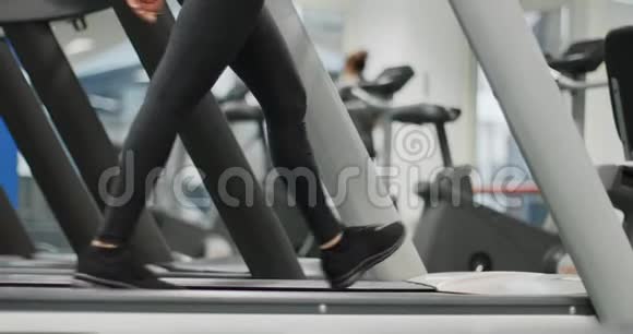年轻女子在健身房跑步机上行走热身或降温腿侧视近景拍摄下身细节妇女视频的预览图