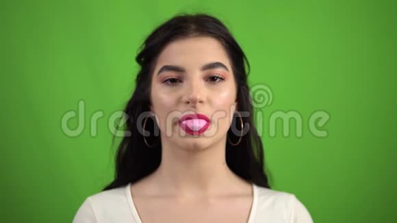 微笑的女孩在绿色的屏幕上吹泡泡糖嚼着粉红色的泡泡糖视频的预览图