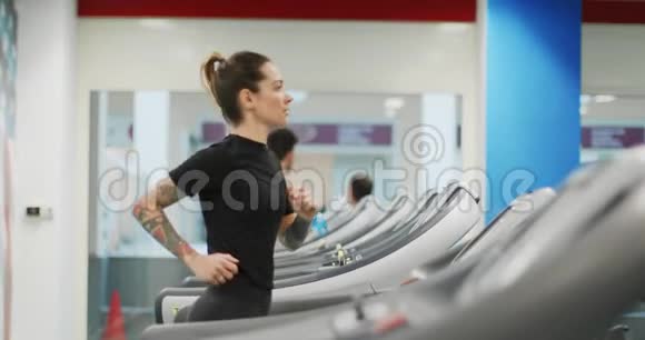 年轻女子在健身房跑步机上跑步侧视健身中心女子训练女性锻炼有氧运动视频的预览图