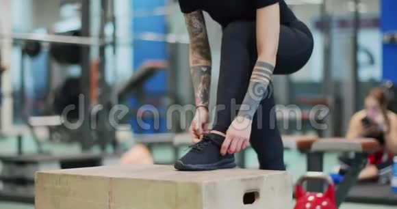 女人在健身房的跳跃箱上系花边女子系鞋带准备腿部训练前景特写慢视频的预览图