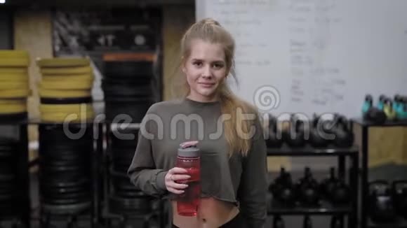 漂亮的金发美女正在从塑料瓶里喝水在健身俱乐部的体操馆里散步视频的预览图