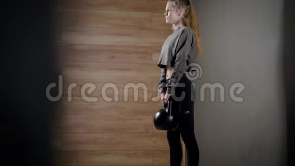 年轻女子蹲在健身馆里手里拿着水壶铃训练背部腿部和手部肌肉视频的预览图