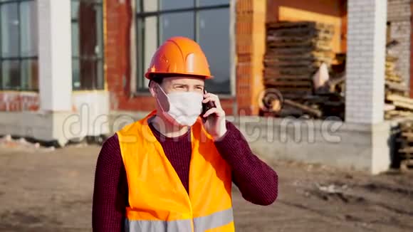 男建筑工人穿着工作服戴着医用口罩在家背景上用手机谈论冠状病毒视频的预览图