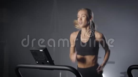 金发女人在黑暗大厅的健身俱乐部里跑步锻炼她的耐力和有氧运动视频的预览图