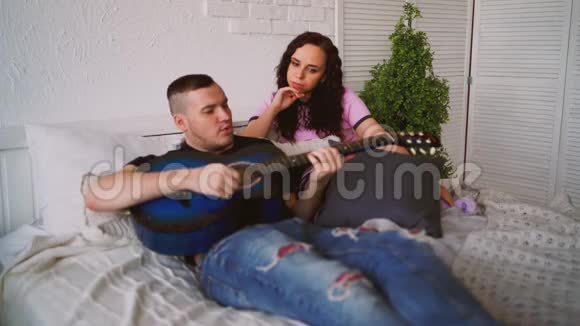 可爱的一对吉他坐在床上男人在床上为你女朋友演奏蓝色的吉他视频的预览图