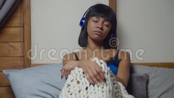 悲伤的女人在床上用耳机听音乐视频的预览图