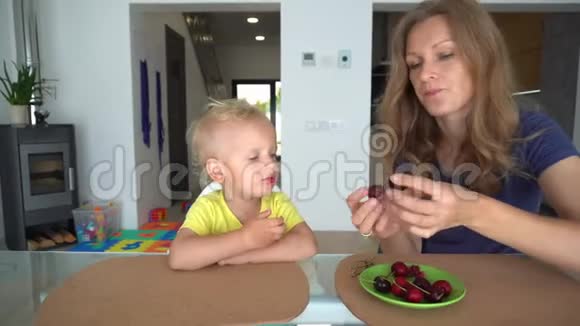 可爱的妈妈在家里给她的孩子喂樱桃浆果妈妈亲儿子视频的预览图