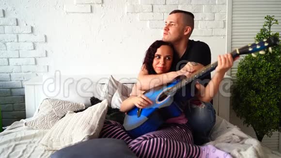 可爱的一对吉他坐在床上男人抱着女友坐在床上弹蓝声吉他视频的预览图