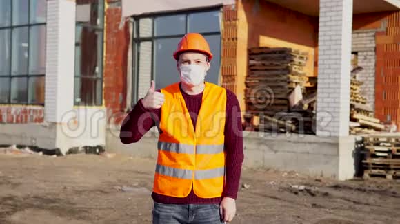 男建筑工人穿着工作服戴着医用口罩在建筑中的房屋背景上竖起大拇指视频的预览图