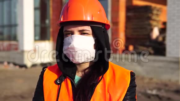 在建房屋背景上佩戴医用口罩和工作服的女建筑工人画像视频的预览图