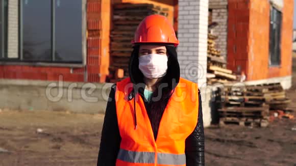 在建房屋背景上佩戴医用口罩和工作服的女建筑工人画像视频的预览图