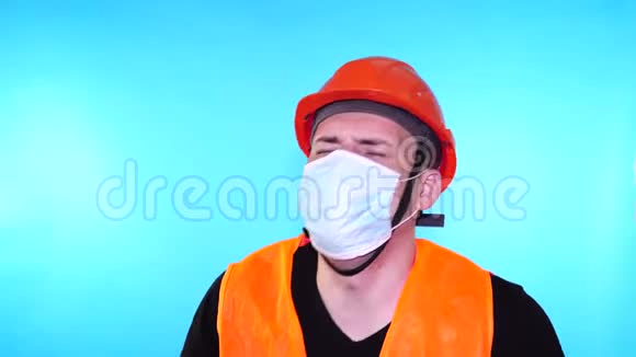 男建筑工人穿着工作服戴着医用口罩蓝底咳嗽感染威胁的概念视频的预览图