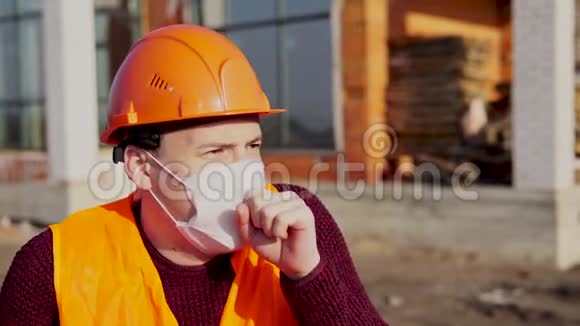 男建筑工人穿着工作服戴着医用口罩在建房屋背景下咳嗽概念视频的预览图