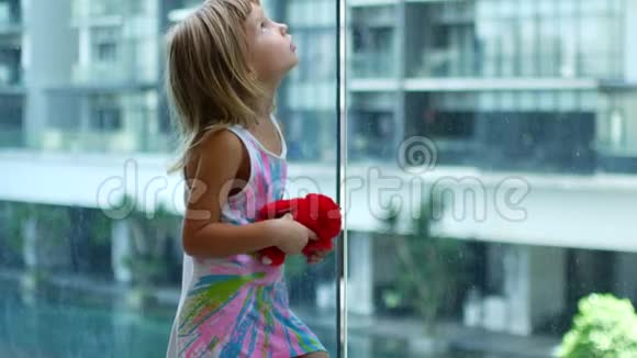 金发小女孩站着转向透明玻璃视频的预览图