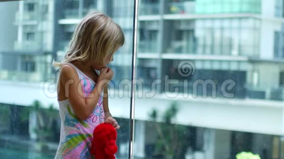 金发小女孩站着转向透明玻璃视频的预览图