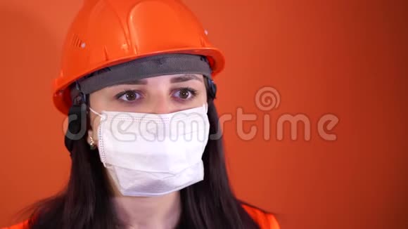 女建筑工人穿着工作服在橙色背景下从脸上摘下医疗面罩视频的预览图