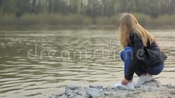 河岸上的一个女孩把一块石头扔进水里从后面看到的视频的预览图