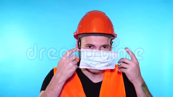 男建筑工人穿工作服在蓝色背景上脸上戴医用口罩视频的预览图