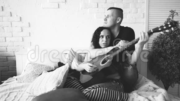 可爱的一对吉他坐在床上男人抱着女友坐在床上弹蓝声吉他视频的预览图