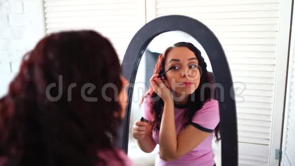 年轻漂亮的女人穿着睡衣在家里照镜子画着睫毛膏与迷人的女性亲密接触视频的预览图
