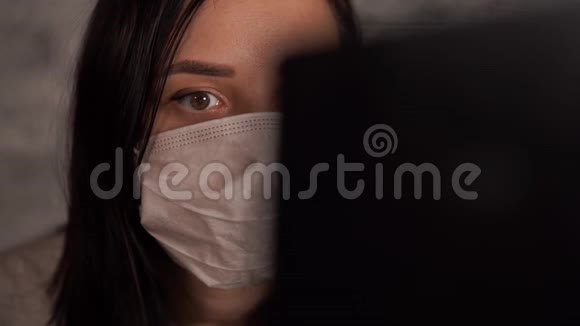 一个戴着医用面具的女人用笔记本电脑从互联网上得知冠状病毒的消息女性关心的是视频的预览图