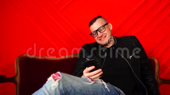 英俊的年轻人戴着眼镜靠在红色的墙上的小沙发上成年笑男坐在扶手椅上视频的预览图