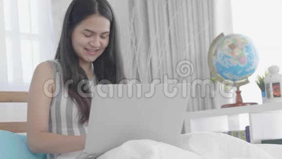 一位年轻的亚洲妇女在家里用带笑脸的笔记本电脑视频的预览图