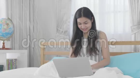 一位年轻的亚洲妇女在家里用带笑脸的笔记本电脑视频的预览图