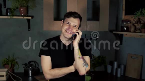 年轻微笑男子在厨房用手机说话的肖像成年迷人的男性一边笑一边说视频的预览图