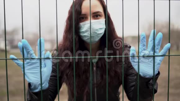年轻女子戴着医用口罩通过栅栏遮住脸成年女性用面具遮住她的脸视频的预览图