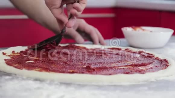 一个年轻人的手把番茄酱贴在比萨饼面团上视频的预览图