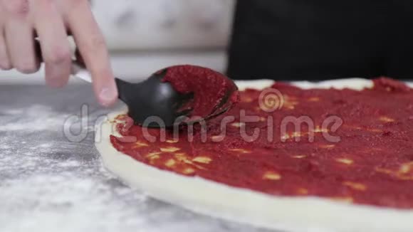 一个年轻人的手把番茄酱贴在比萨饼面团上视频的预览图