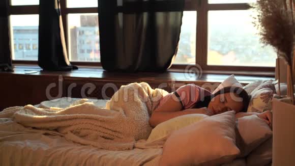 清晨睡在格子布下枕头上的年轻女子成年女性醒来打哈欠看着时间视频的预览图